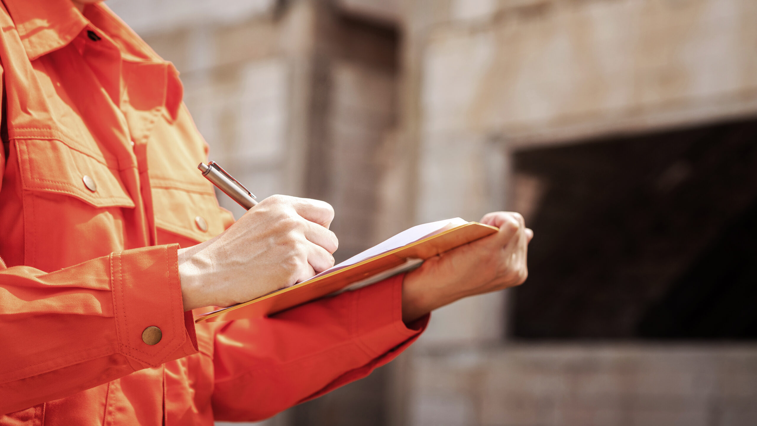 Person in orange jacket writing on clipboard.