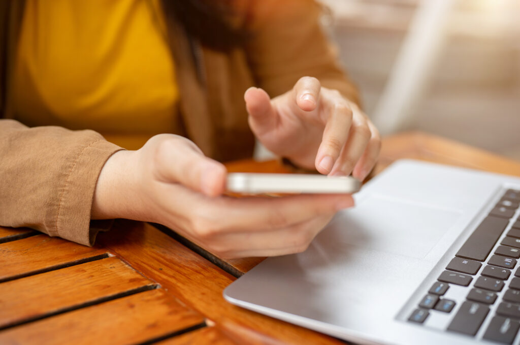 Person using smartphone and laptop at table.