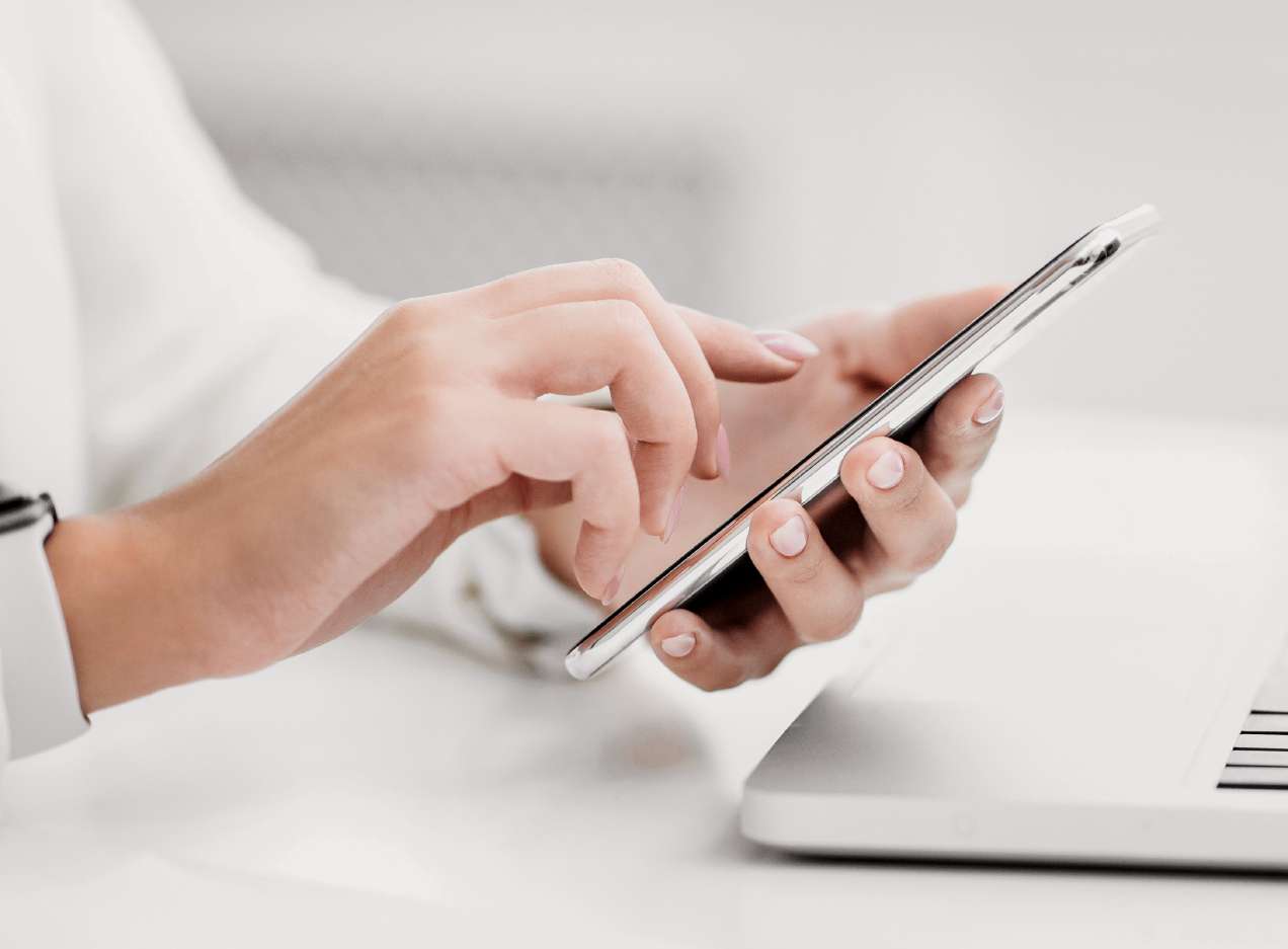Close-up of hands using smartphone near laptop