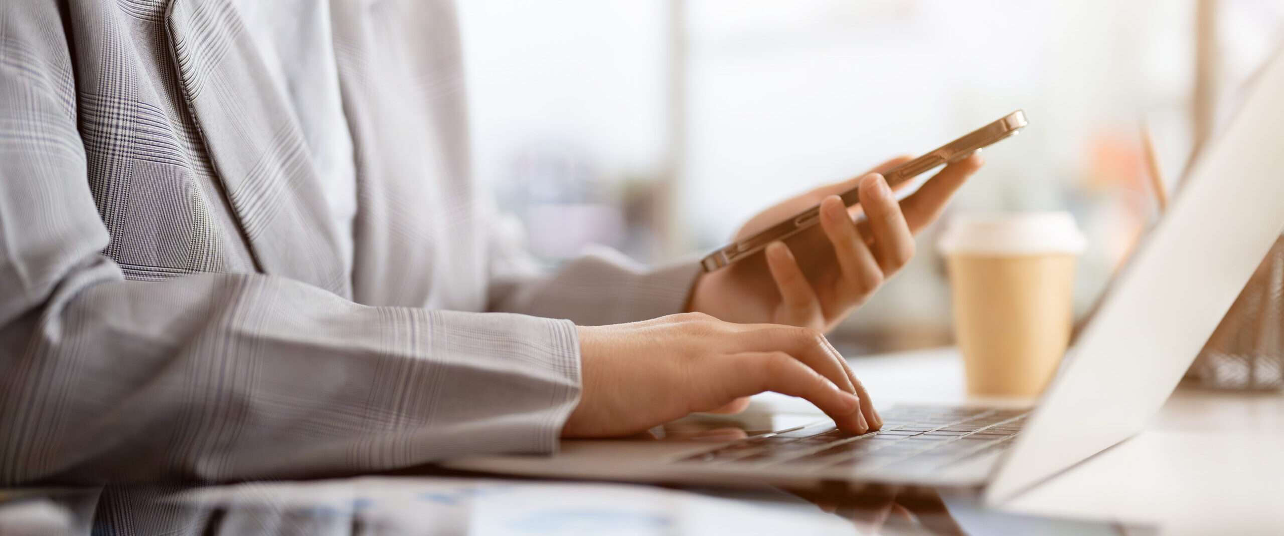 Hands typing on laptop while holding smartphone